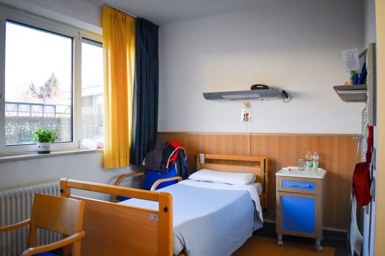 Camera di degenza con letto, comodino e ampia finestra
